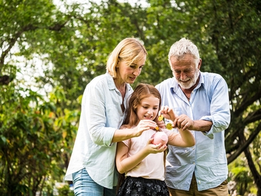 Kind steht mit Großeltern im Garten und wirf Geld in eine Sparschwein