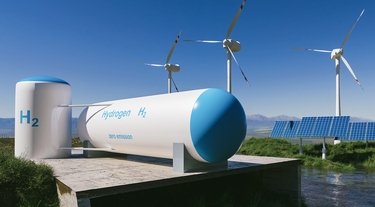 Wasserstofftanks sind im Vordergrund zu sehen. Im Hintergrund stehen drei Windräter und PV-Anlagen
