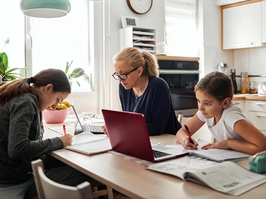 Arbeitenden Mutter sitzt mit ihren zwei Kindern am Küchentisch, die Hausaufgaben machen 