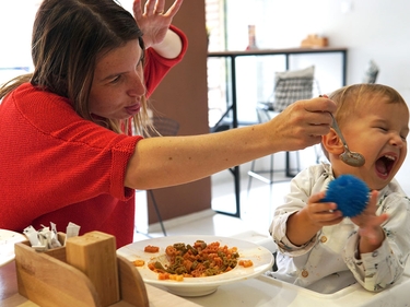 Weinendes Kind weigert sich, zu essen, während Mutter versucht, das Kleinkind durch Tricks zu täuschen