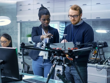 Ingenieurin und Ingenieu arbeiten an einem Drohnenprojekt mit Hilfe von Laptop und Notizen. 