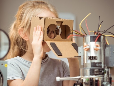 Kind hält sich eine selbgebastelte VR-Brille aus Pape vor die Auge 