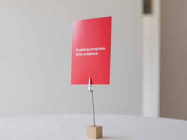 Auf einem Tisch steht eine rote Karte mit dem Prognos-Claim: Enabling progress. With evidence. 