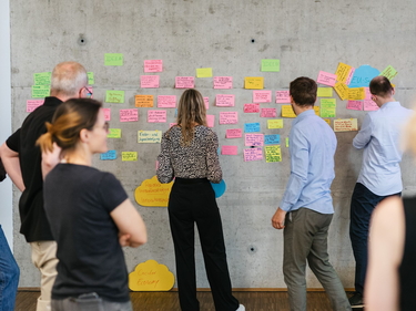 Eine Gruppe von Personen stehen an einer Wand und lesen PostIts 