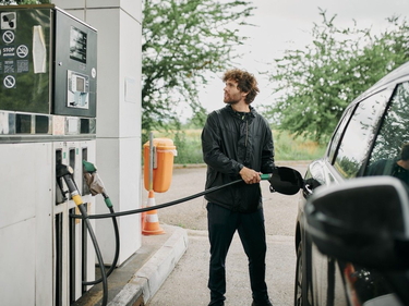 Mann steht an Zapfsäule und tankt sein Auto