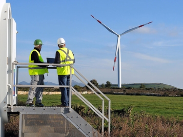 Zwei Ingenieure stehen auf einem Feld mit Windkraftanlage