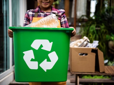 Mädchen trägt eine Tonne mit Recyclingsymbol 