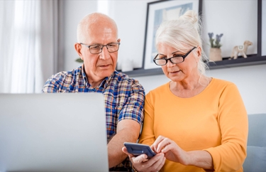 Zwei Senioren benutzen Laptop und Smartphone
