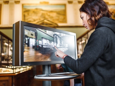 Junge Frau bedient einen Touchscreen-Monitor im Museum 