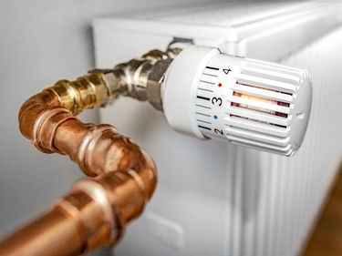 Nahaufnahme eines weißen Heizkörperthermostats mit Kupferrohr