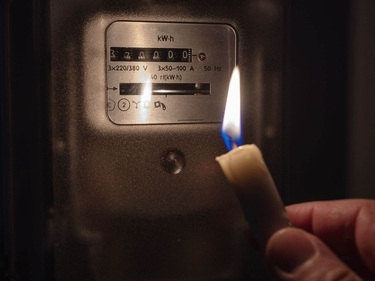 Mensch prüft Stromzähler im Kerzenlicht