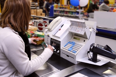 eine junge Kassiererin scannt Produkte an eine Supermarktkasse