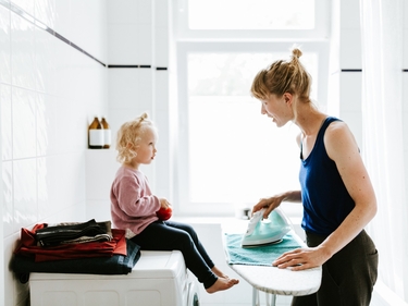 Mutter betreut Kind und bügelt ein Handtuch