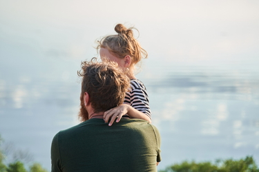 Ein Vater blickt mit seinem Kind im Arm auf das Meer.