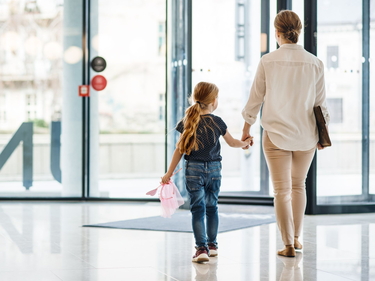 Mutter und Tochter, die Hand und Hand aus einem Büro hinausgehen