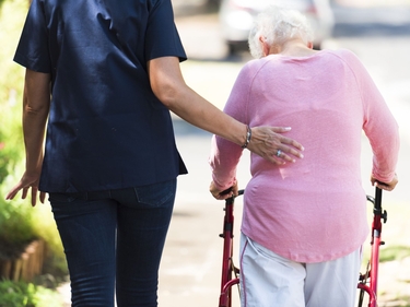 Seniorin geht an einem Rollator, Pflegefachkraft stützt sie 