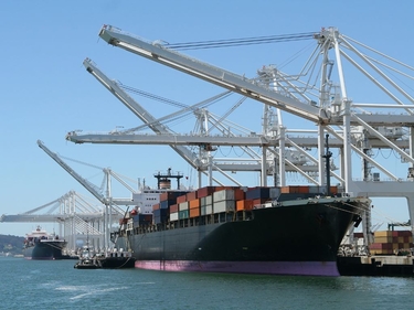 Ein großes Containerschiff wird von Kränen im Hafen mit Containern beladen.