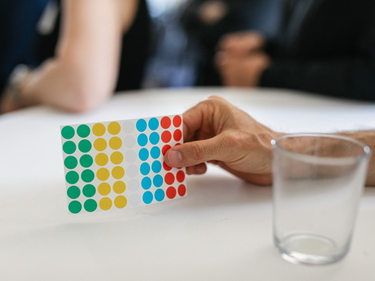 Eine Hand hält einen Zettel mit Klebepunkten für ein Meeting.