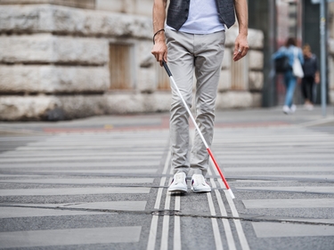 Blinder Mann mit weißem Stock geht zu Fuß über die Straße in der Stadt