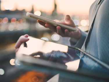 Nahaufnahme von einem Tablet und Handy in der Hand einer Person. Im Hintergrund sieht man eine Stadt.