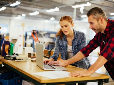 Zwei Personen stehen in einer Arbeitssituation am Laptop