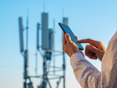 Internetmast, davor eine Hand die ein Handy hält