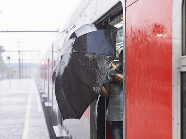 Roter Zug am Bahnhof, es regnet, Person steigt mit einem Regenschirm ein