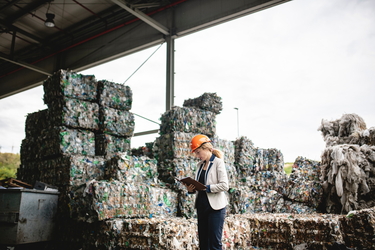 Eine Mitarbeiterin steht auf einer Deponie vor Abfällen mit einem Tablet