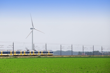 ein Zug fährt auf einer Strecke zwischen grünem Feld und Windkraftwerk