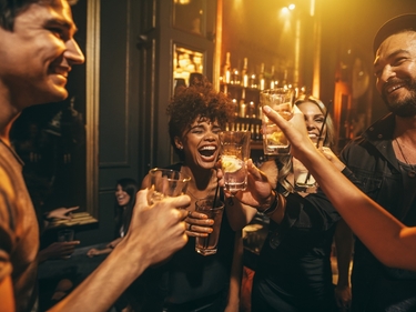 Menschen lachen ausgelassen in einer Bar und stoßen an