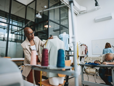 EIne Modesignerin arbeitet in einem Atelier an einer Schneiderpuppe.