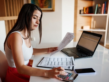 Junge Frau mit Rechnungen vor ihrem Laptop