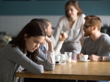 Trauriges Mädchen sitzt mit anderen Menschen an einem Tisch