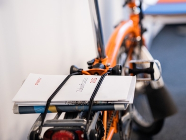 Zeitungen sind auf den Gepäckträger eines orangefarbenen Fahrrads geklemmt