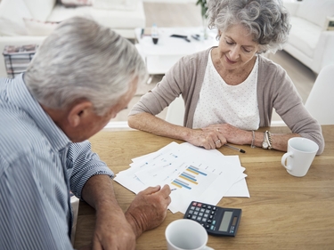 Rentnerin und Rentner am Tisch mit Taschenrechner und Statistiken