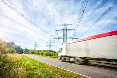 LKW fährt auf der Straße, im Hintergrund Strommaste