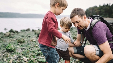 Vater sammelt Steine am Wasser mit seinen zwei Kindern