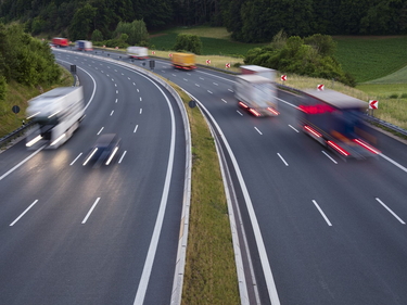 Mehrspurige Autobahn mit schneller Verkehrsspur, Fahrzeuge als Lichtspuren im Dämmerlicht.
