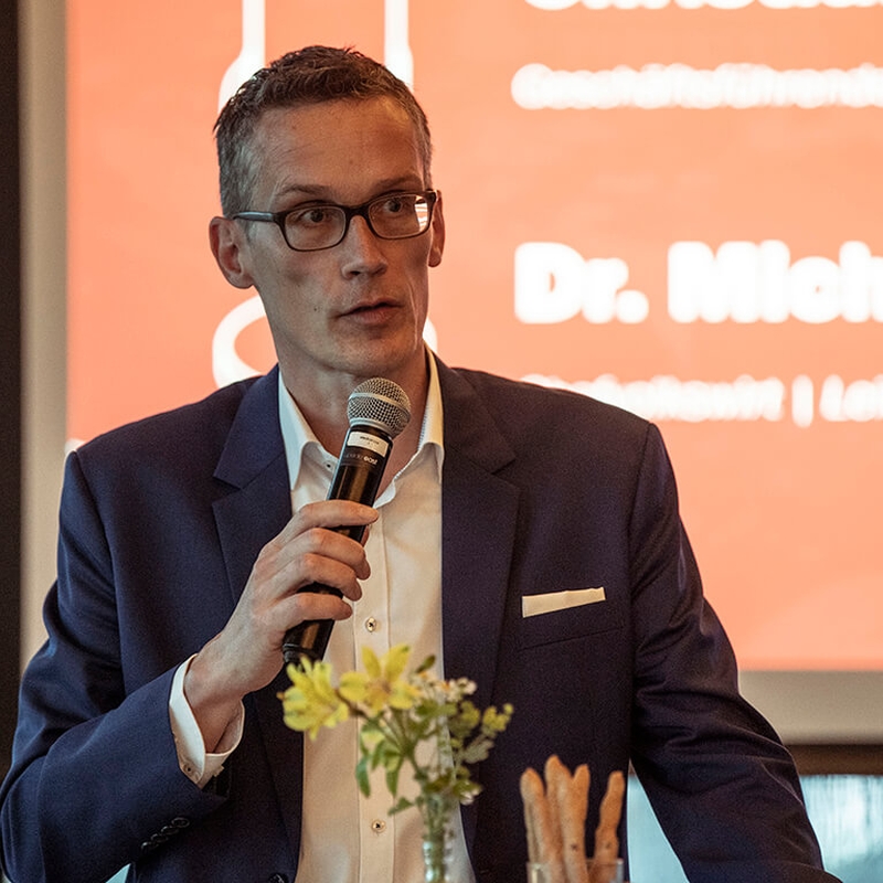 Michael Böhmer mit Mikrofon vor einer Leinwand, auf der ein Vortrag zu sehen ist