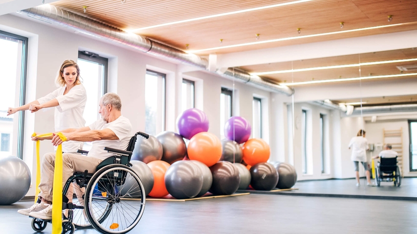unge Frau Physiotherapeut arbeitet mit einem älteren Mann im Rollstuhl