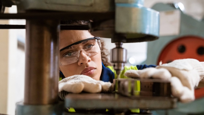Weibliche Ingenieurin mit Schutzbrille arbeitet an einer Fertigungsanlage.