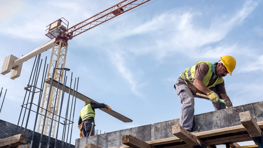 Bauarbeiter auf einer Baustelle, im Hintergrund ein großer Kran