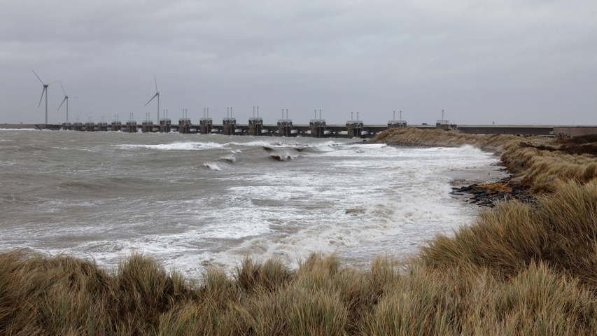 Dünen, wildes Meer mit hohen Wellen und im Hintergrund eine geschlossene Sturmsperre