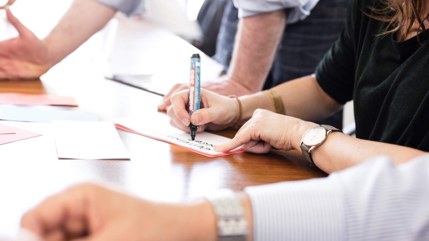 Drei Personen schreiben während eines Workshops auf Karten und diskutieren