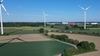 Regionalzug fährt durch eine unbebaute Landschaft, im Hintergrund Windräder