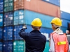 Zwei Personen mit Schutzhelmen schauen auf Frachtcontainer und tauschen sich aus. 