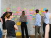 Eine Gruppe von Personen stehen an einer Wand und lesen PostIts 