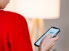 Person mit rotem Pulli hält Smartphone in der Hand