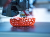 Ein 3D-Drucker druckt ein rotes Gefäß mit Löchern. 