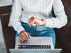 Frau sitzt auf dem Sofa mit einem Laptop auf den Beinen und schaut auf die Uhr